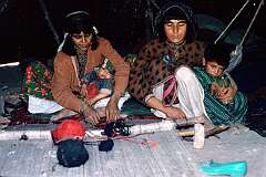 Women of the nomadic Kuchi people are expert carpet weavers and, while looking after their children, are at work in their black tent on the outskirts of Herat.
