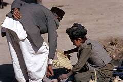 A man is buying kebabs from a boy on a street market in the bazaar of Kandahar.