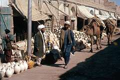 The main street of Kandahar, a bustling place with open-fronted shops and street vendors. This is the area where pottery is sold. Camels are a valuable means of transport.