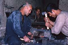 Beating the iron while it's hot in a smithy in Mazar. The boy in the background operates the bellows to blow air on the fire.