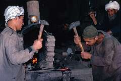 Beating the iron while it's hot in a smithy in Mazar. The man in the background operates the bellows to blow air on the fire.