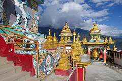 View to the large prayer wheel, small chortens and statues of the Buddha and bodhisattva, from the steps into the temple underneath the giant Buddha statue.