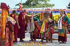 A monk presents a “khata” ceremonial scarf to a masked spiritual king.