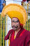 A monk with ceremonial headdresses and face paint to keep order with long staves, at the Torma ritual.