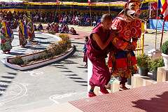 A masked dancer at the Drub-chod-Chen-Mo Torgya returns up the steps to the main hall of the monastery accompanied by a monk.