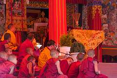 Novice monks on the terrace in front of the main entrance of the monastery during a ritual with a monk singing prayers.