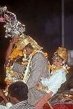 The bridegroom with a young boy behind him on a Ghodi, a white horse, adorned with embellishments to match the groom, now with a headdress, in his Baraat Hindu wedding procession.