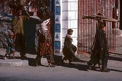 Women from a nearby village, carrying heavy loads, walking with their children.