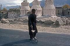 A boy rolling a hoop past old chortens in Thikse.
