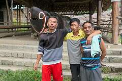 Three Naga men in front of a "Süngkong", the Ao name for the log drum, in Kisama Naga Heritage Village.