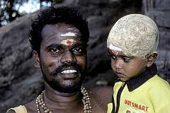 A father and his young son, his head shaved as devotion to the god Shiva and covered with tumeric in Palani.