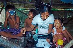 Marlyna at a sewing machine, with children at home in Tuarabu.