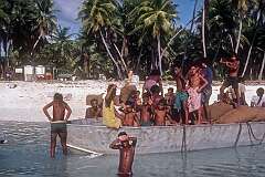 The dinghy carrying bags of copra, with local boys on top of it, off the beach in Taribo.