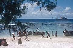 Carrying bags with supplies from the dinghy on the beach of Bakaka,  with the ship “Nei Momi” anchored offshore.